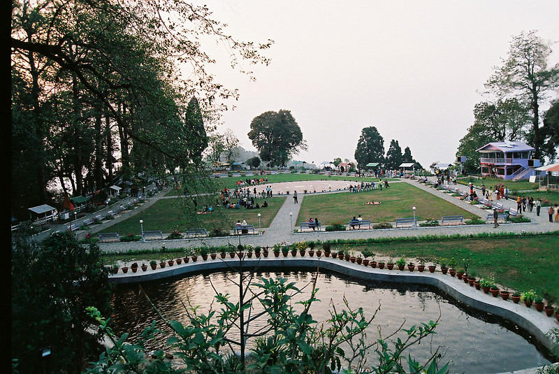 Landscaped Nightingale park with circular lawn, pond in foreground, benches, and people relaxing at sunset.