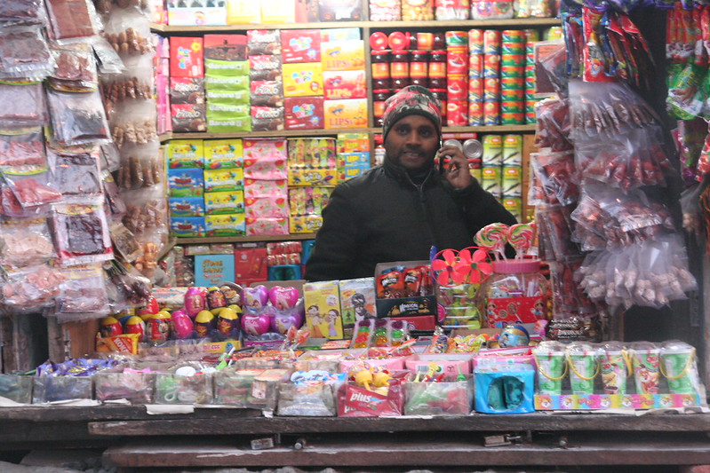 Shopkeeper at a colorful roadside stall displaying souvenirs and snacks among popular things to buy in Darjeeling.