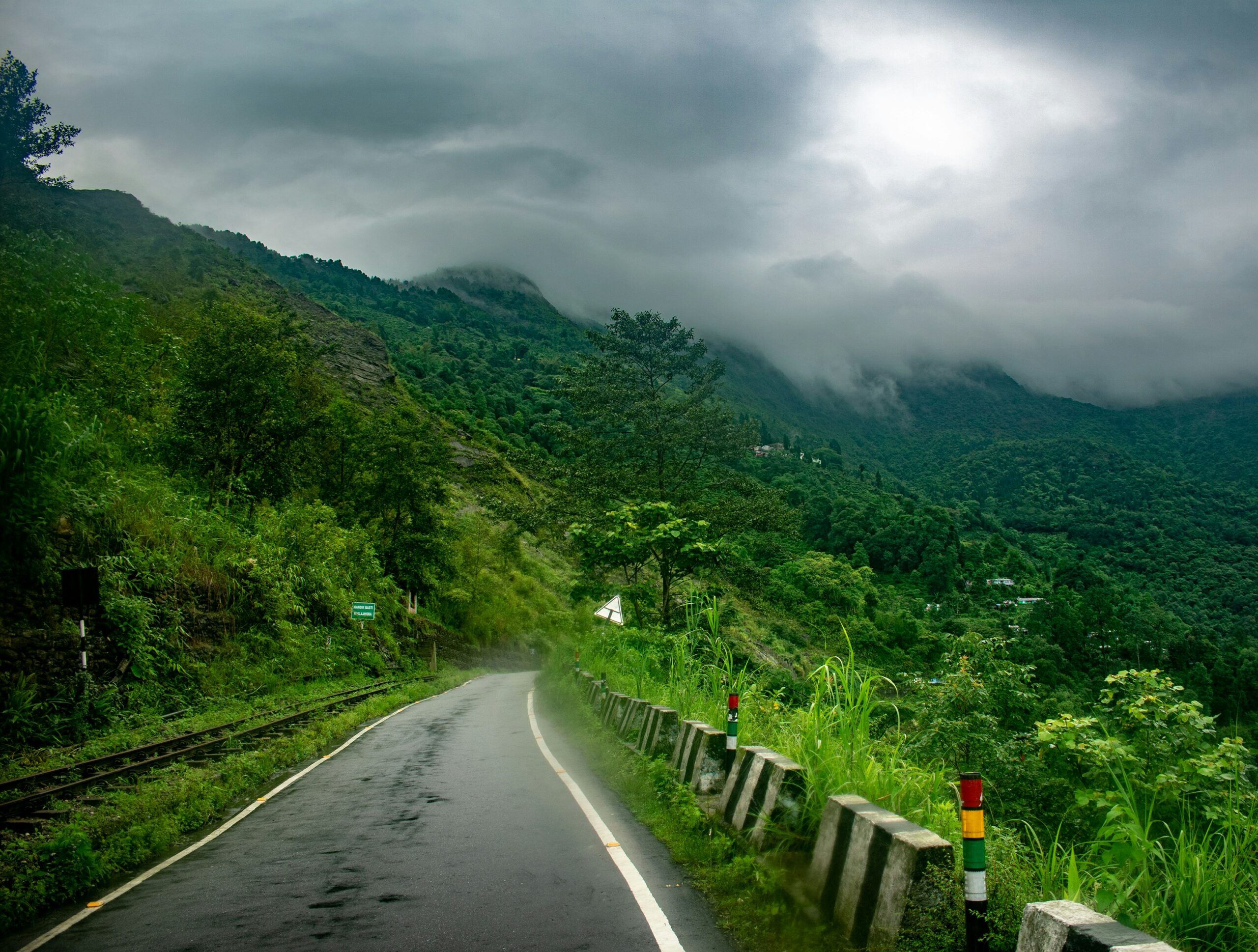 Winding mountain road with lush green hills and misty clouds in Darjeeling.