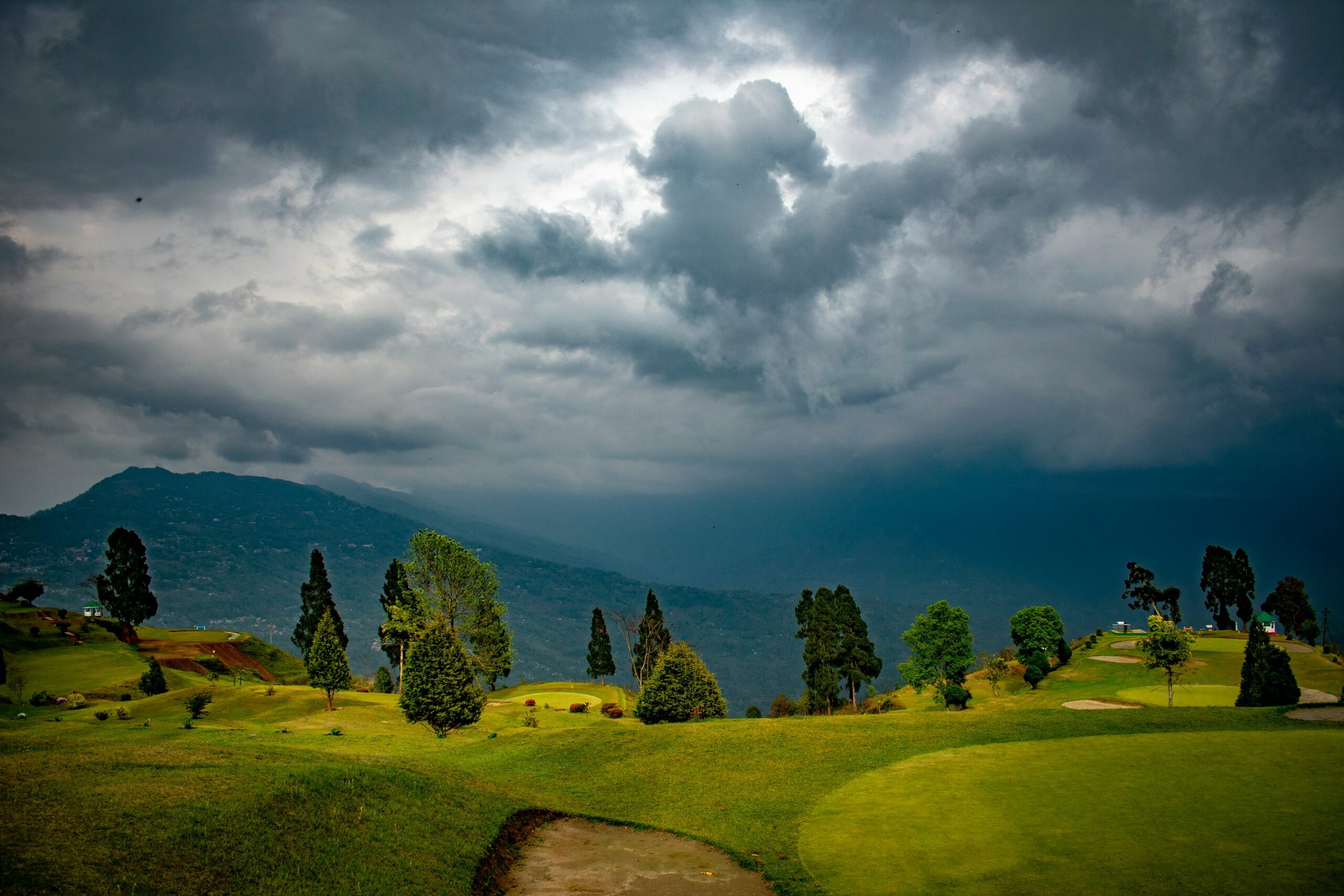 Storm clouds above green golf course with hills and trees in Darjeeling.