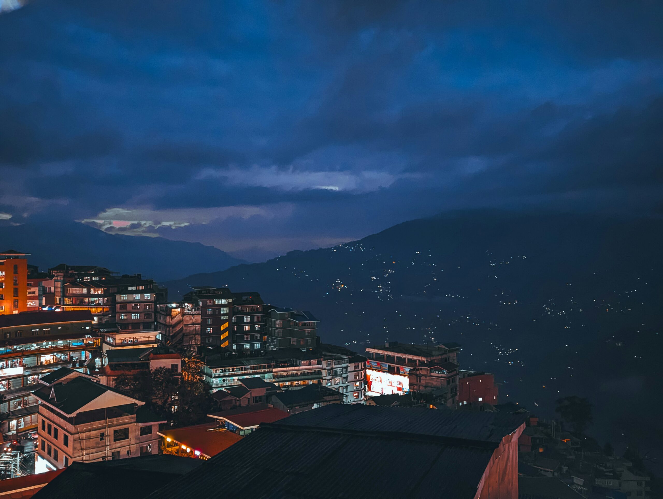 Illuminated hillside buildings and misty mountains at night in Darjeeling.
