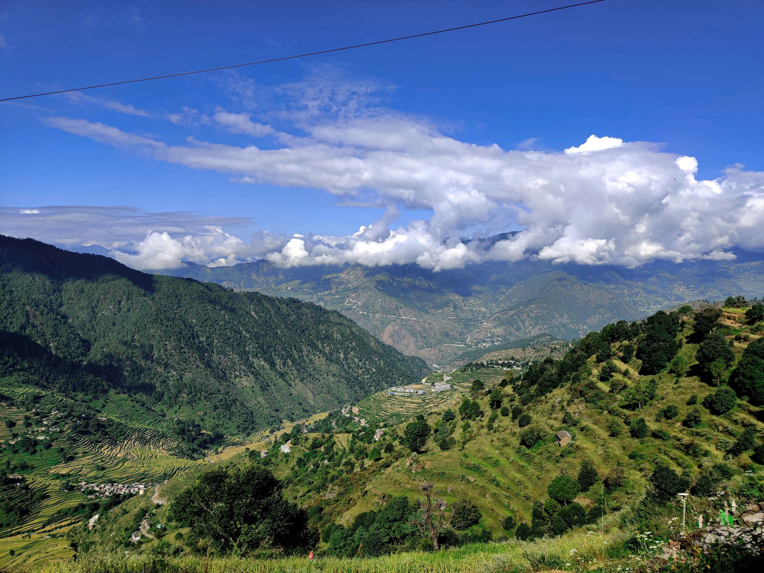 Wide view of lush green mountains, terraced fields, and clouds over Darjeeling hills.