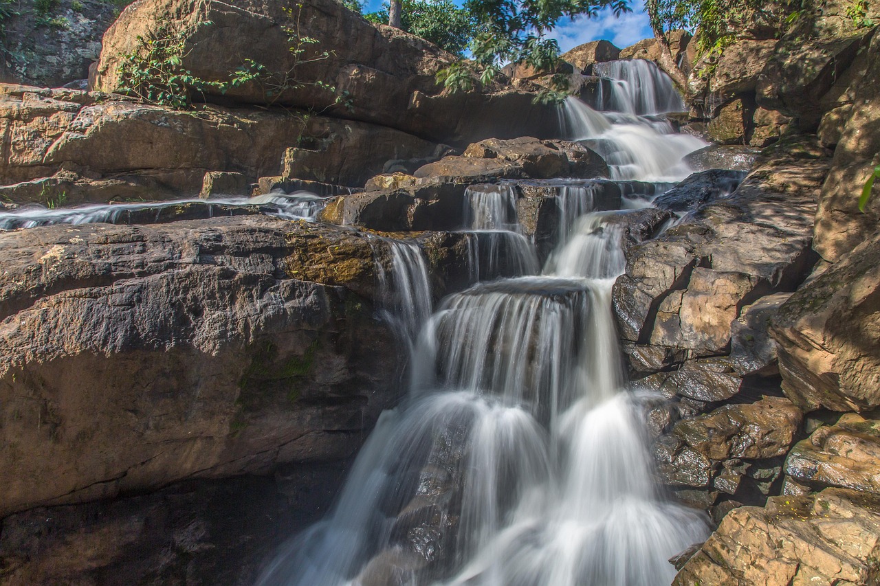 Cascading waterfall flowing over layered rocks surrounded by greenery in a natural forest landscape.