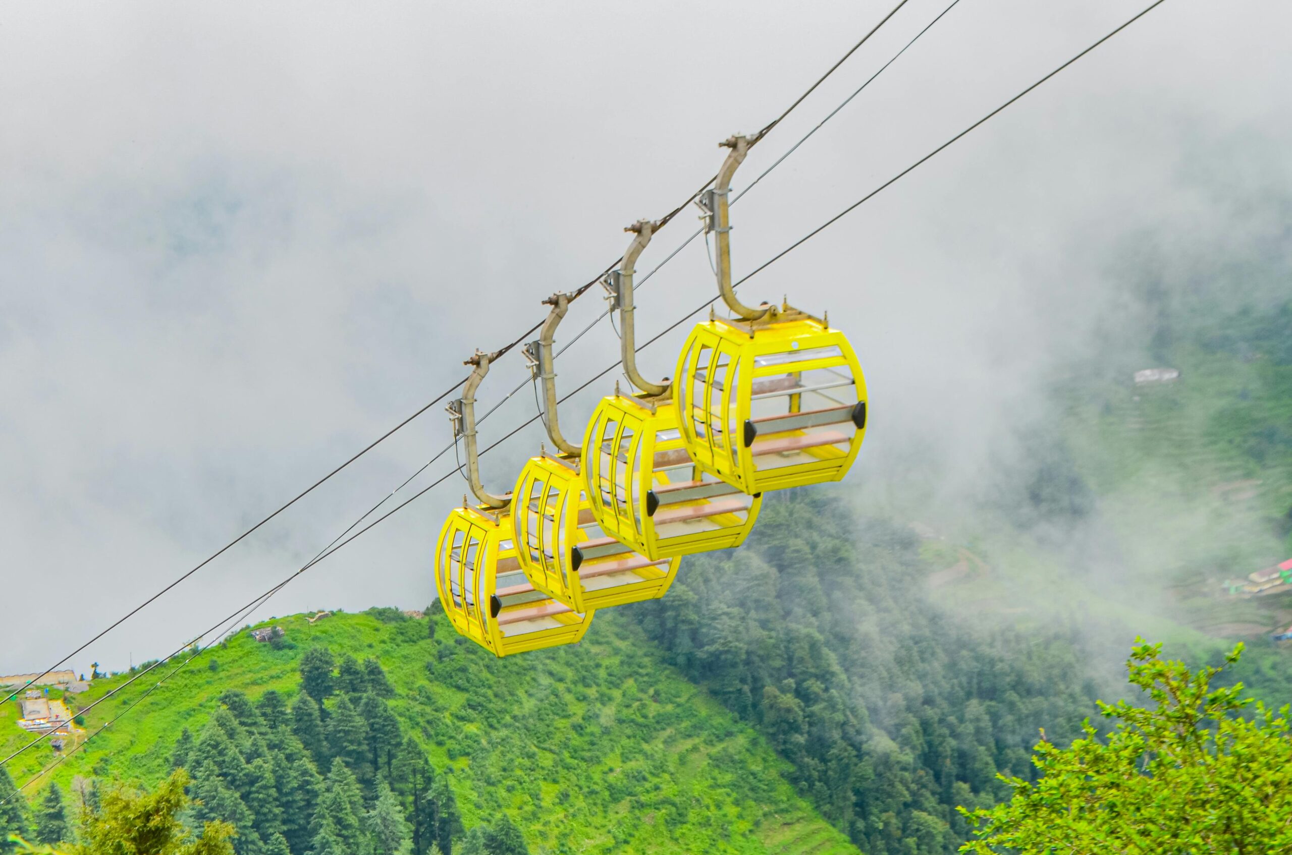 Cable car in Darjeeling moving above green hills and misty mountains with scenic valley views.