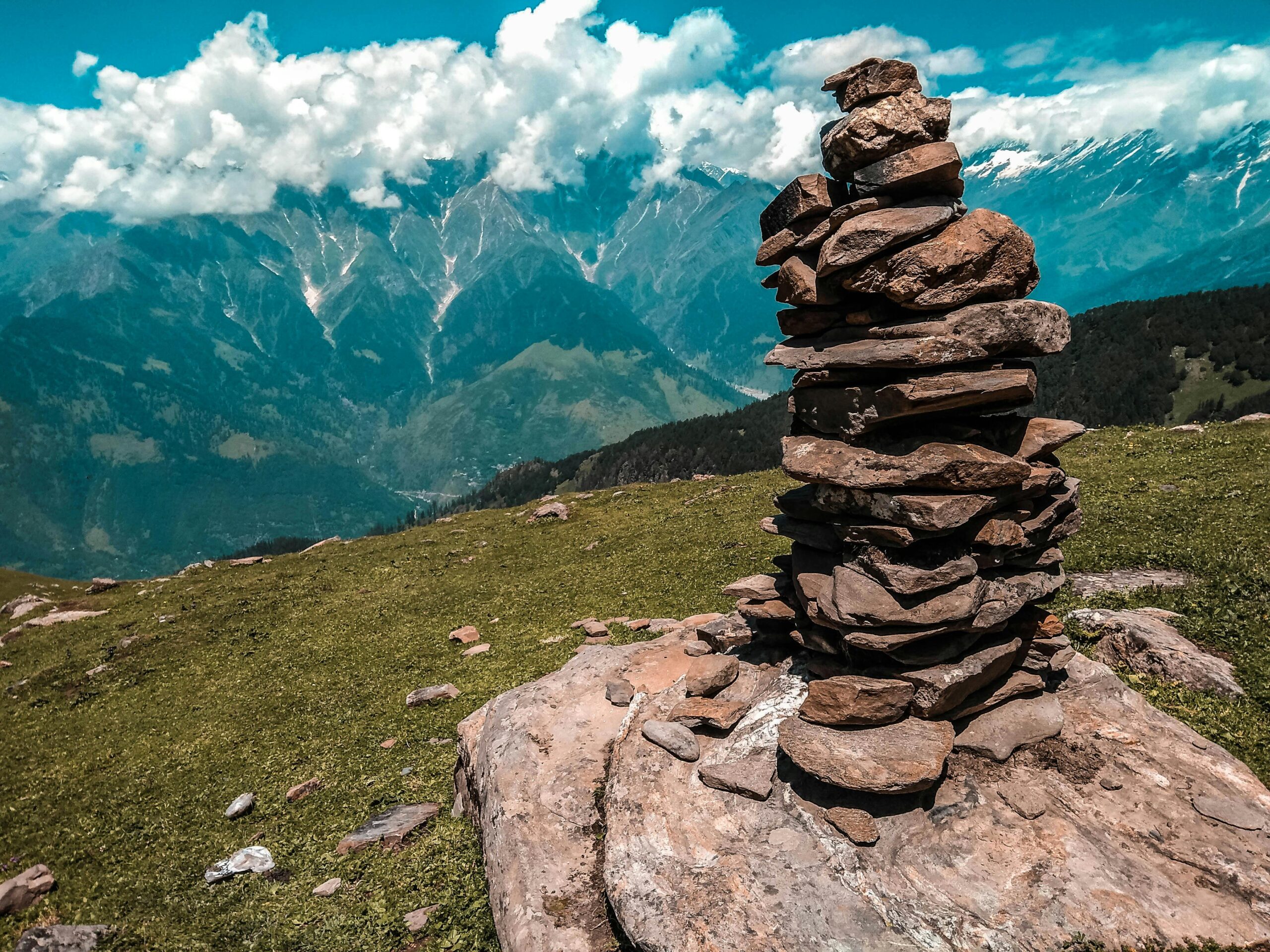 Stone cairn on a grassy hill with Himalayan mountain landscape and clouds in Darjeeling.